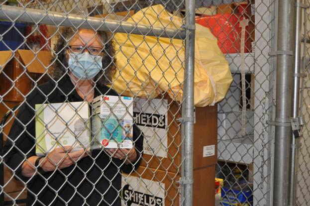 Nan Grottanelli stands in her namesake Nan’s Cage in the Supply Chain warehouse at DCH Regional Medical Center. She is holding N95 and surgical face masks.